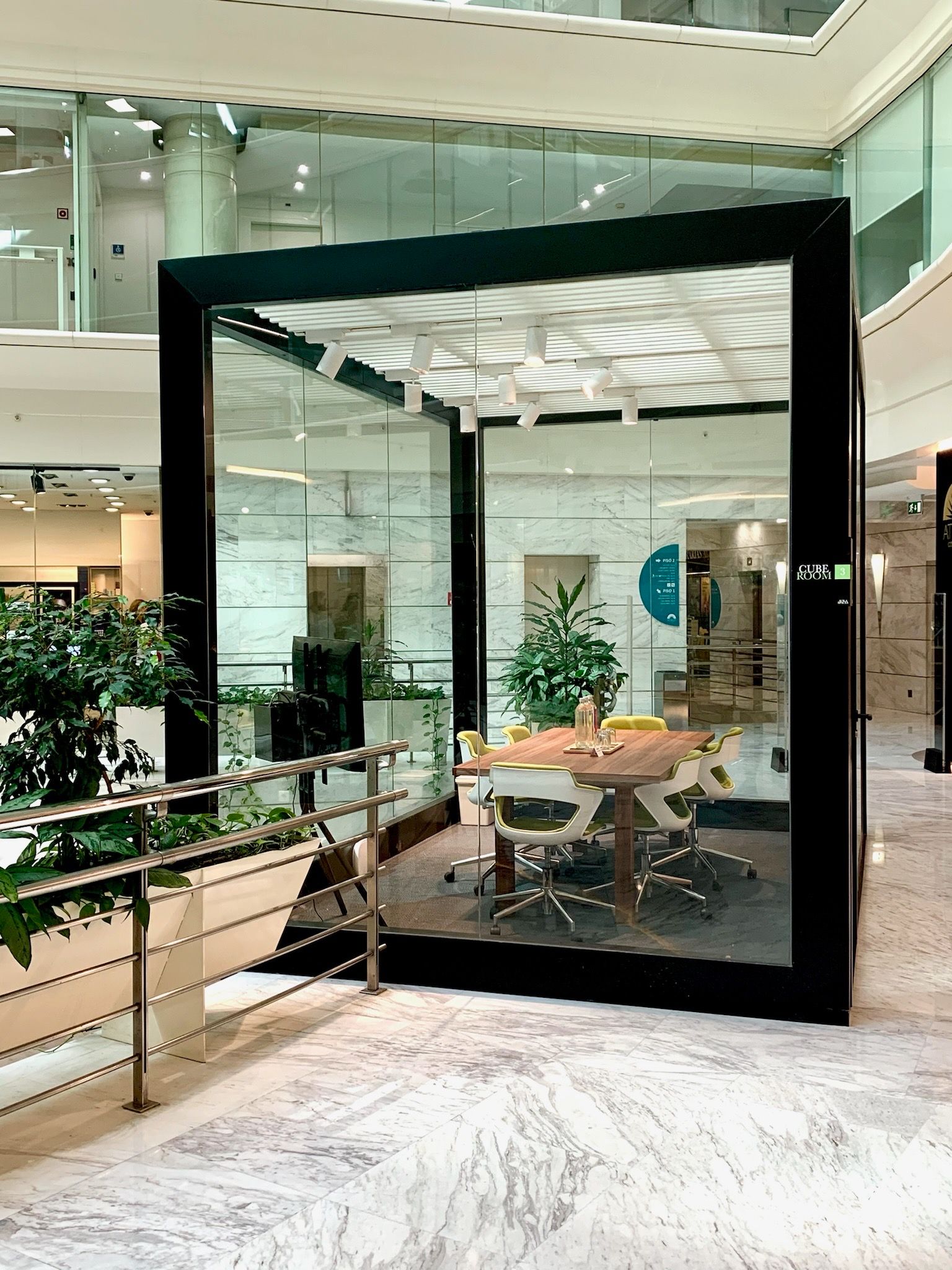 Glass-enclosed cubic meeting room interior mall Lisbon with chairs, boardroom desk and refreshments