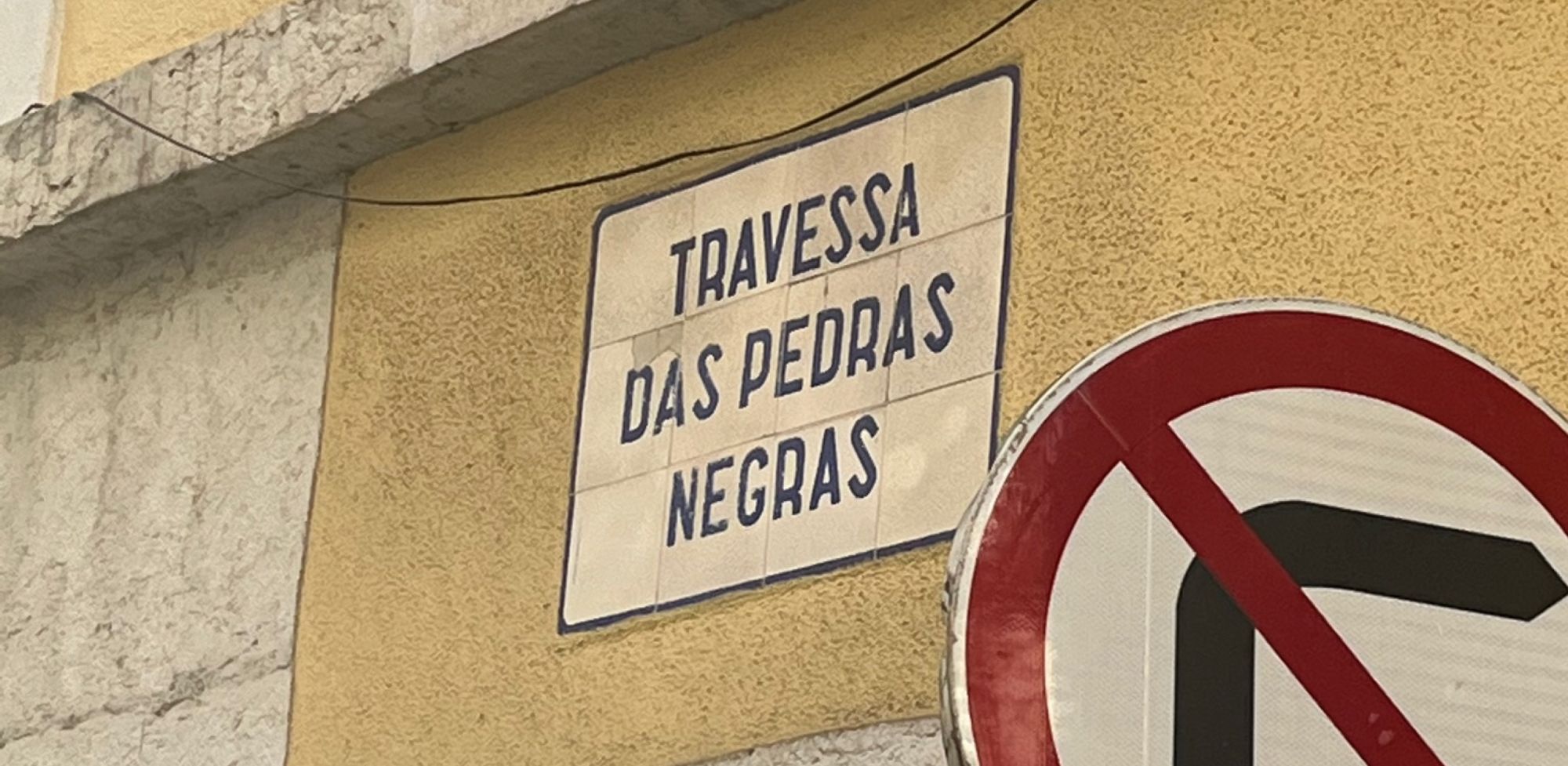 Sign indicating "Travessa das pedras negras" on exterior wall of Lisbon building
