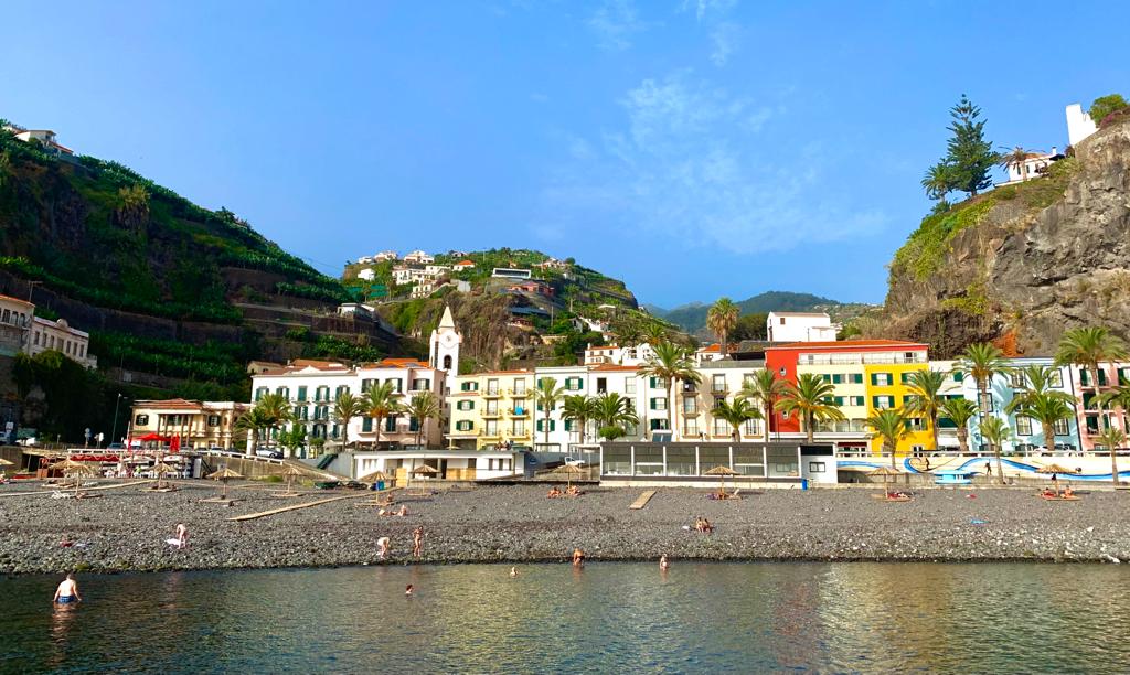 Shoreline of Ponta do Sol with row of buildings, palm trees and hills bracketing the view