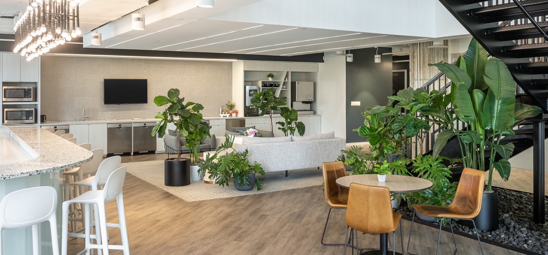 Interior coworking with plants, kitchen, TV, bar-style seating and stairs to second floor