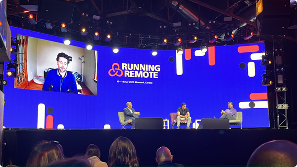 A panel of speakers sit in chairs on the stage of Running Remote in Montreal. The screen is blue.