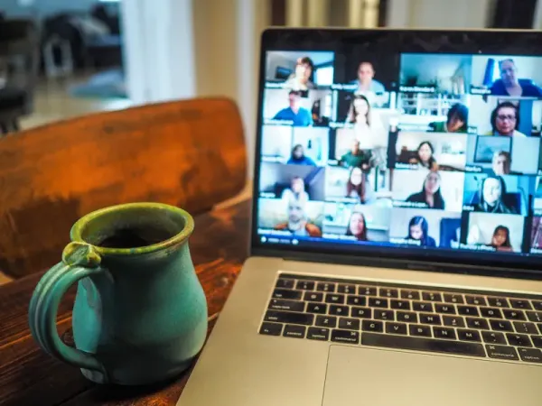 A group of people are seen on a group chat on a laptop. The computer is next to a green mug with a handle.