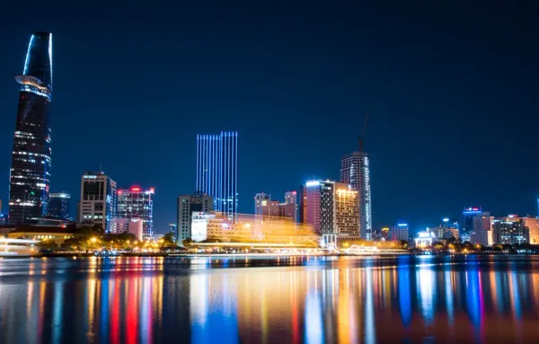 A night sky over Ho Chi Minh city with glass and steel lit-up skyscrapers and buildings reflecting hues on the water